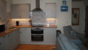 Una cocina compacta con electrodomésticos integrados, un sofá gris y un salpicadero de azulejos.