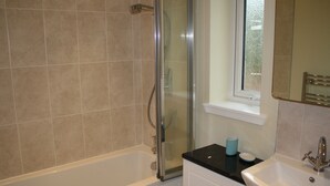 Un baño con ducha acristalada, bañera blanca y lavamanos con espejo.