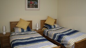 Un dormitorio doble con dos camas, cada una con ropa de cama a rayas y cabeceros de madera, una mesita de noche con lámpara y un cuadro enmarcado en la pared.