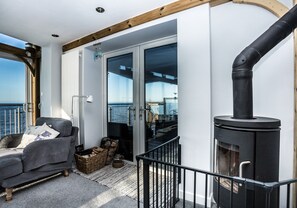 A balcony with a sofa, a fireplace, and a view of the sea.
