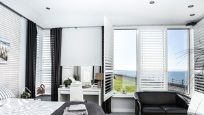 Una camera da letto moderna con un letto, una scrivania, una sedia e ampie finestre con tende.