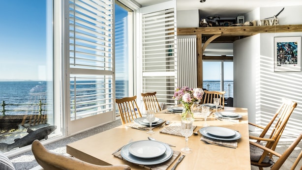 Zona pranzo con vista sull'oceano, arredi in legno e tavolo imbandito per quattro persone.