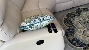 A beige sectional sofa with a built-in TV and remote controls, a patterned throw pillow, and a decorative rug. - Upstairs 3 BR, 2 bath home, 150 yds from beach with beautiful clear water. (Port Royale, South Bimini)