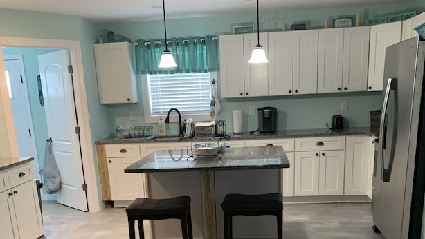 A modern kitchen with white cabinets, a granite countertop, two bar stools, pendant lights, and a refrigerator. - Upstairs 3 BR, 2 bath home, 150 yds from beach with beautiful clear water. (Port Royale, South Bimini)