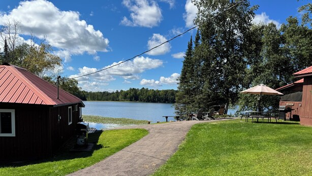 A lakeside property with a paved walkway, a barbecue area, and a small cabin. - Cozy cabin on Island Lake (Winter)