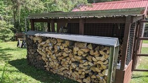 A covered outdoor area with a stack of firewood and a wooden structure with a metal roof. - Cozy cabin on Island Lake (Winter)