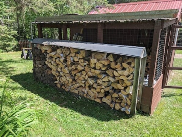 Een overdekt buitengebied met een stapel hout en een houten constructie met een metalen dak.