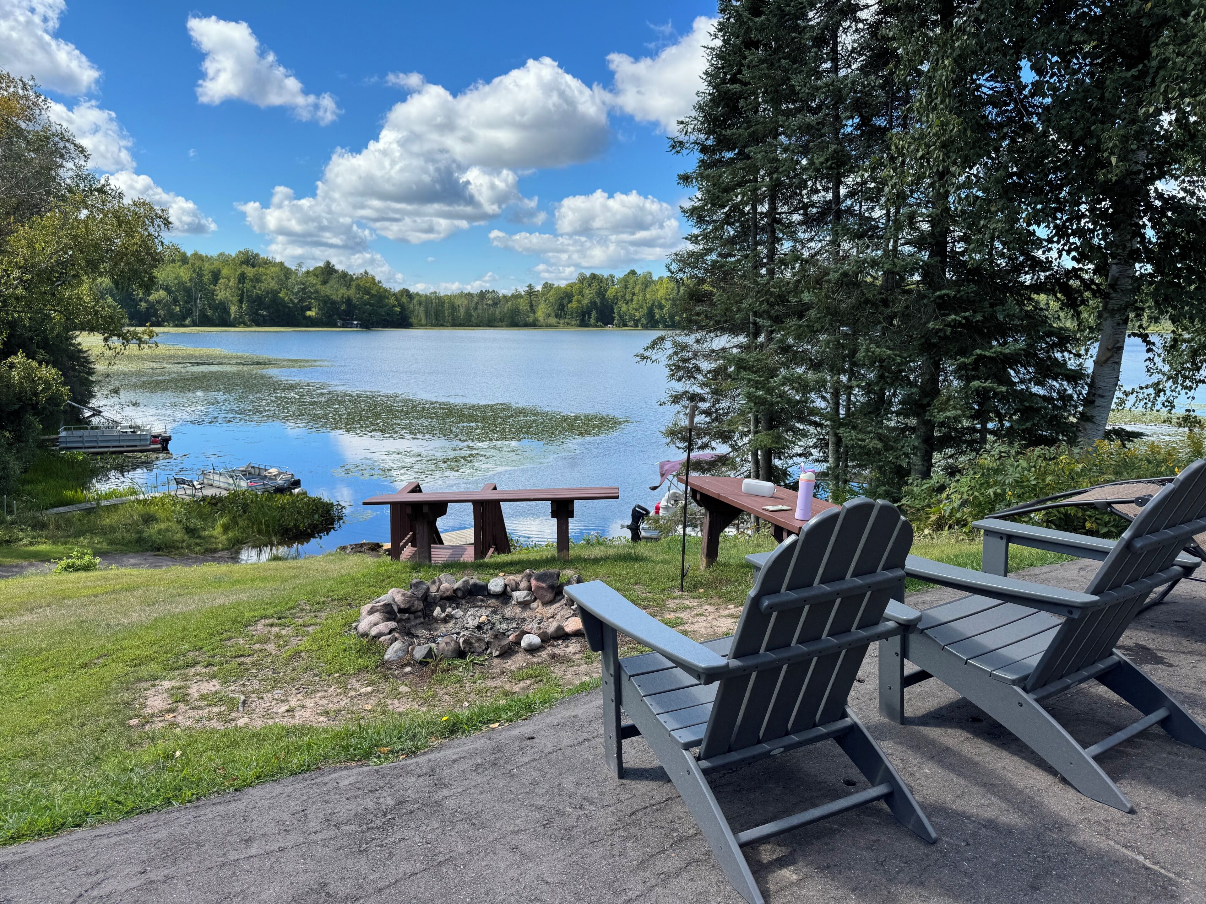 Un espace de détente aménagé au bord du lac, avec des fauteuils Adirondack, une table de pique-nique et un quai avec des bateaux.