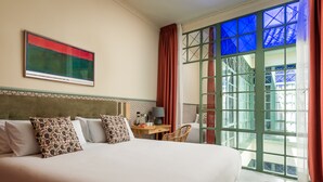 Une chambre d’hôtel avec un grand lit, un bureau avec une lampe et une vue par une fenêtre encadrée de vert.
