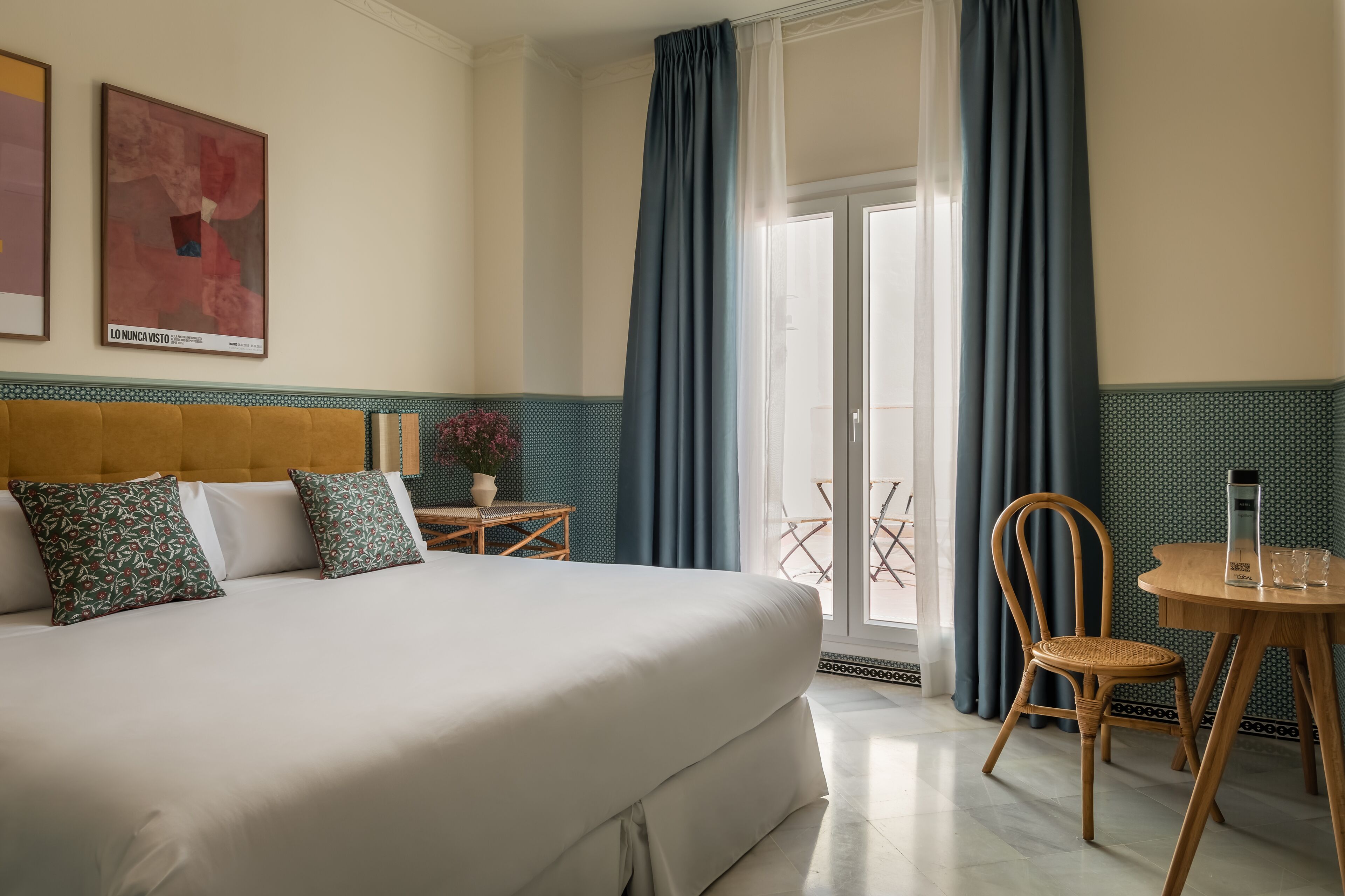 Ein Hotelzimmer mit einem großen Bett, einem Holzstuhl, einem kleinen Tisch und Blick durch eine Glastür nach draußen.