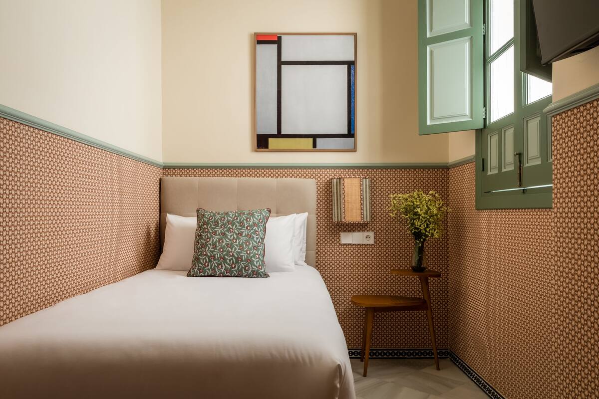 Una habitación de hotel con una cama, una mesita con un florero y una obra de arte colgada en la pared.