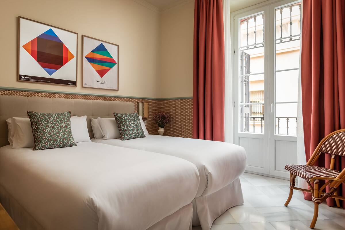 Una habitación de hotel con dos camas, una silla de madera y dos cuadros enmarcados en la pared.