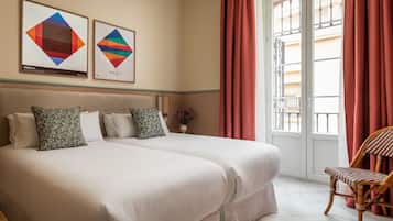 Una habitación de hotel con dos camas, una silla de madera y dos cuadros enmarcados en la pared.