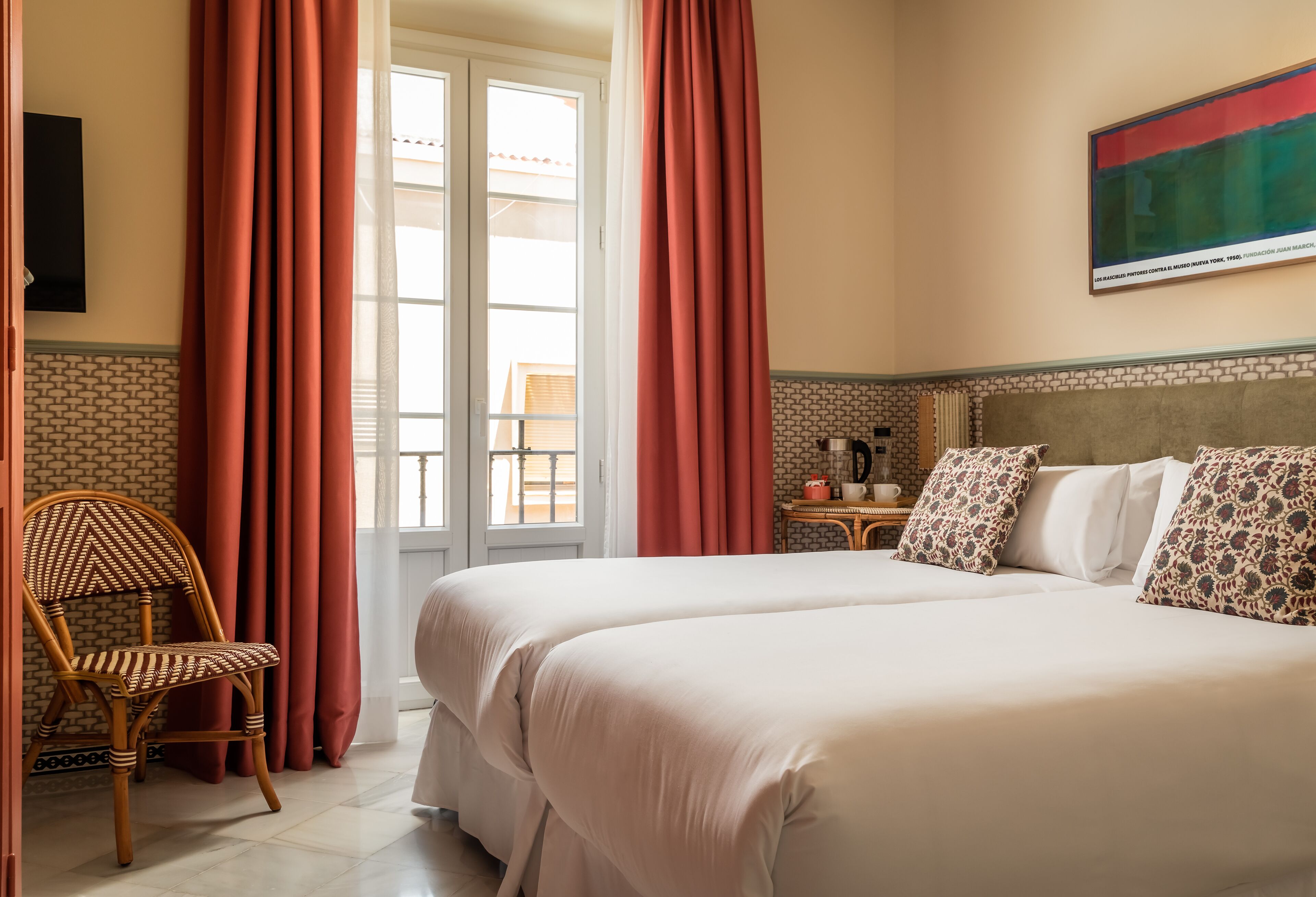 Een hotelkamer met twee bedden, een houten stoel, een klein tafeltje met een waterkoker en een schilderij aan de muur.