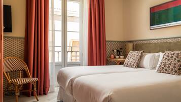 Een hotelkamer met twee bedden, een houten stoel, een klein tafeltje met een waterkoker en een schilderij aan de muur.