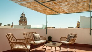 Une terrasse sur le toit, aménagée avec des meubles en osier, une petite table et offrant une vue sur un bâtiment historique en arrière-plan.
