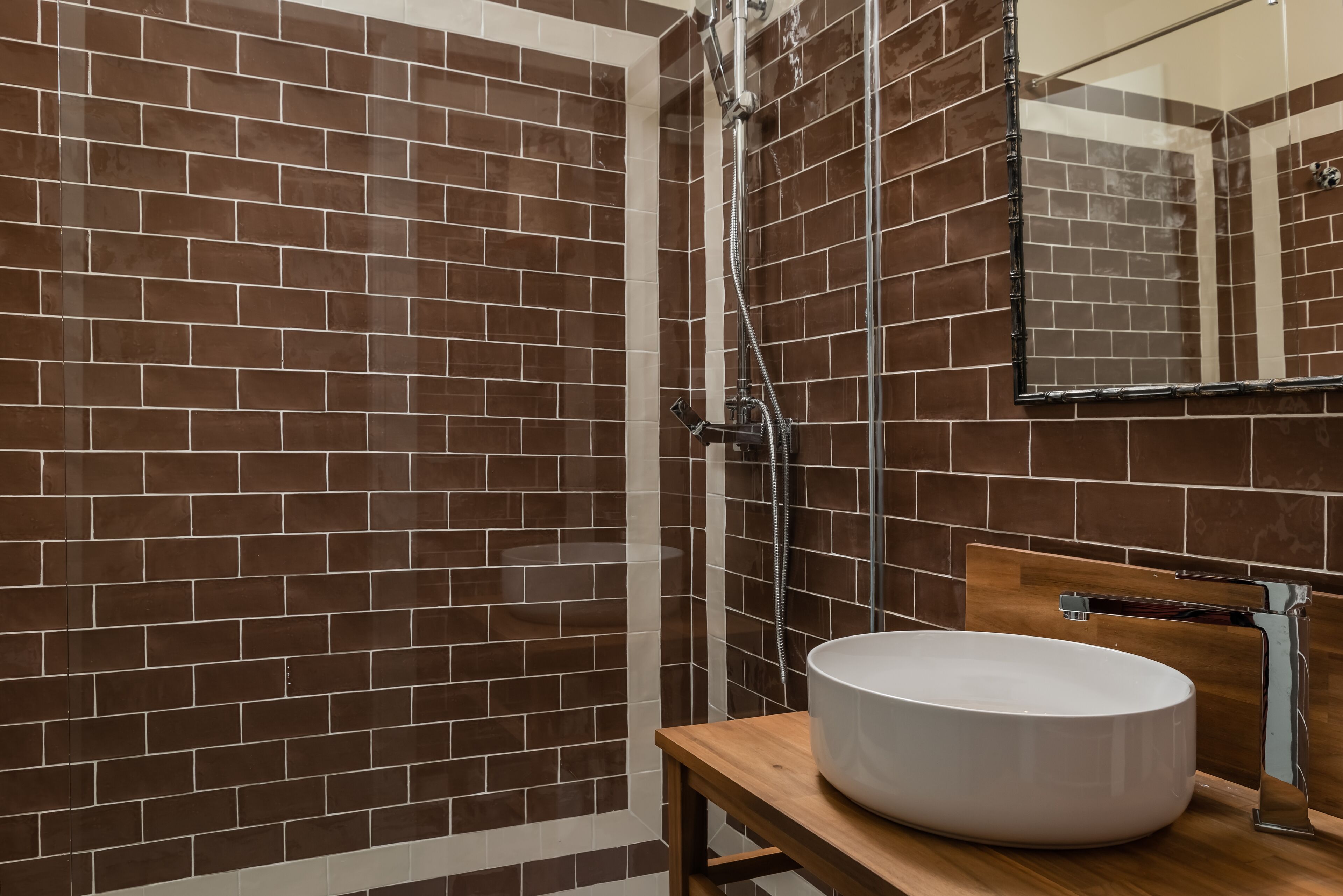 Une salle de bain avec des murs recouverts de carreaux marron, un meuble-lavabo en bois et un lavabo blanc.