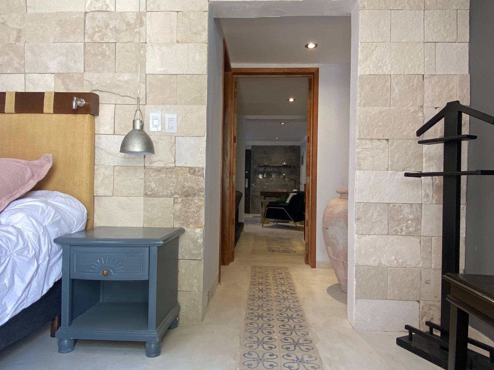A bedroom with a bed, nightstand, lamp, and a hallway leading to a dining area.