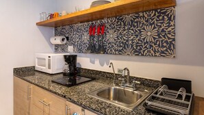 A kitchen with a granite countertop, a stainless steel sink, a microwave, a coffee maker, and a dish drying rack.