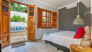 A bedroom with a bed, wooden doors, a hanging light fixture, and a view of greenery outside. - Casa Dali, A+ location lovely house Paseo Montejo (Centro)