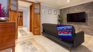 A modern living room with a dark sofa, a flat-screen TV mounted on the wall, and a wooden door leading to another room. - Casa Dali, A+ location lovely house Paseo Montejo (Centro)