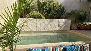 A pool area with a stone wall, potted plants, and striped cushions.