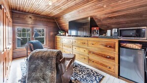 A cozy cabin interior with a wooden ceiling, a large wooden dresser, a microwave, and a refrigerator.