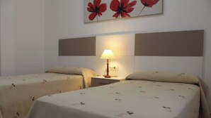 A hotel room with two single beds, a nightstand with a lamp, and a wall with a floral painting. - Apartment - Standard Floor - Without Terrace (Raxó)