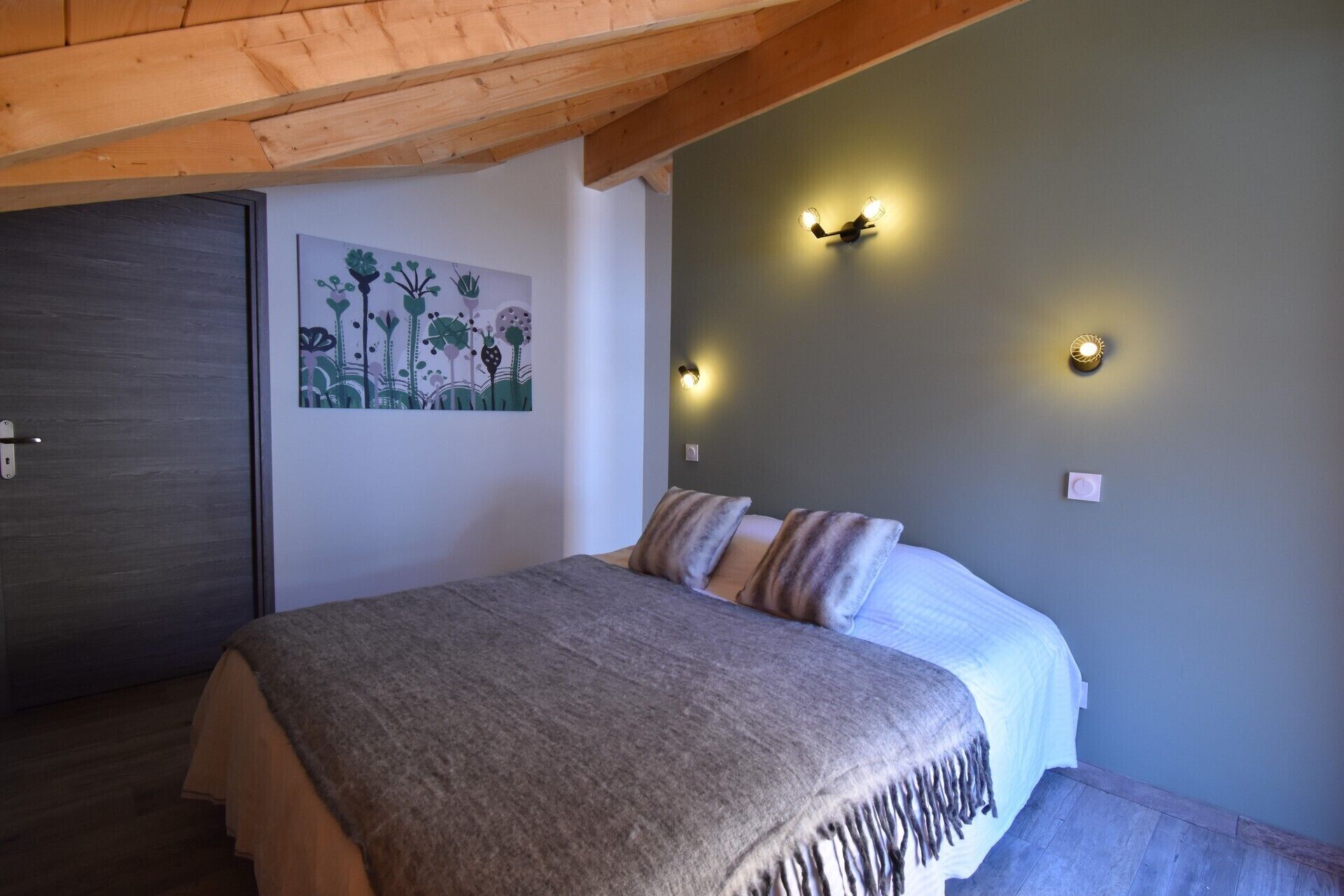 Une chambre à coucher avec un lit, un plafond en bois, un mur orné d’un tableau et des lampes fixées au mur.