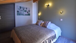 A bedroom with a bed, a wooden ceiling, a wall with a painting, and wall-mounted lights.