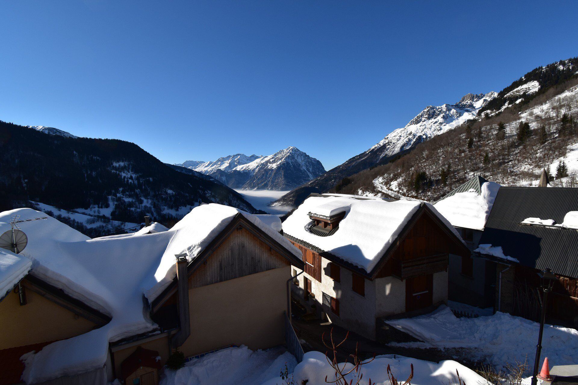 Un pueblo cubierto de nieve en la montaña con casas de madera tradicionales, cielo despejado y un valle con montañas al fondo.