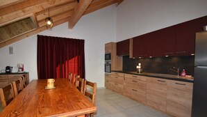 A modern kitchen with wooden cabinets, a large dining table, and a red curtain.