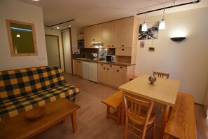 A compact living space with a sofa, a dining table with chairs, a kitchen area with cabinets and appliances, and a small window. - CLARET 2 APPARTEMENT 6 (Vaujany)