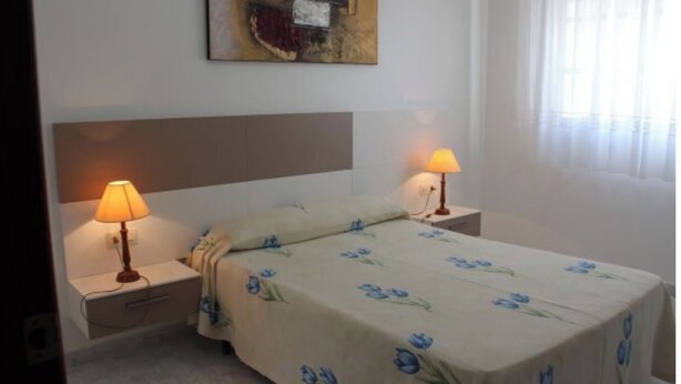 A hotel room with a bed, two bedside tables with lamps, a wall-mounted painting, and a window with curtains. - Apartment - Ground Floor - without terrace (Raxó)