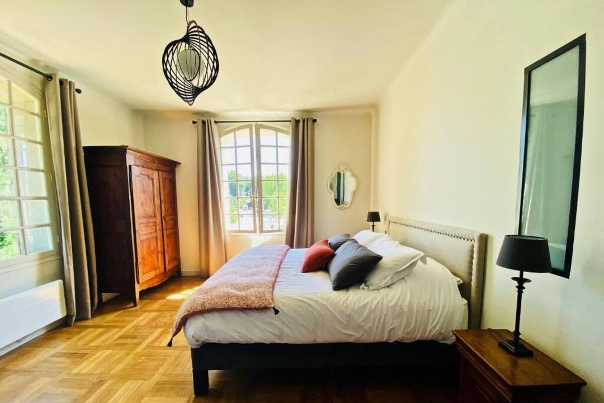 Un dormitorio con cama, suelo de madera, un armario, un espejo y una ventana con cortinas.