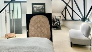 A modern bedroom with a large bed, a chair, and a desk. There are skylights and a framed picture on the wall. - Villa Agrippa (Orange)