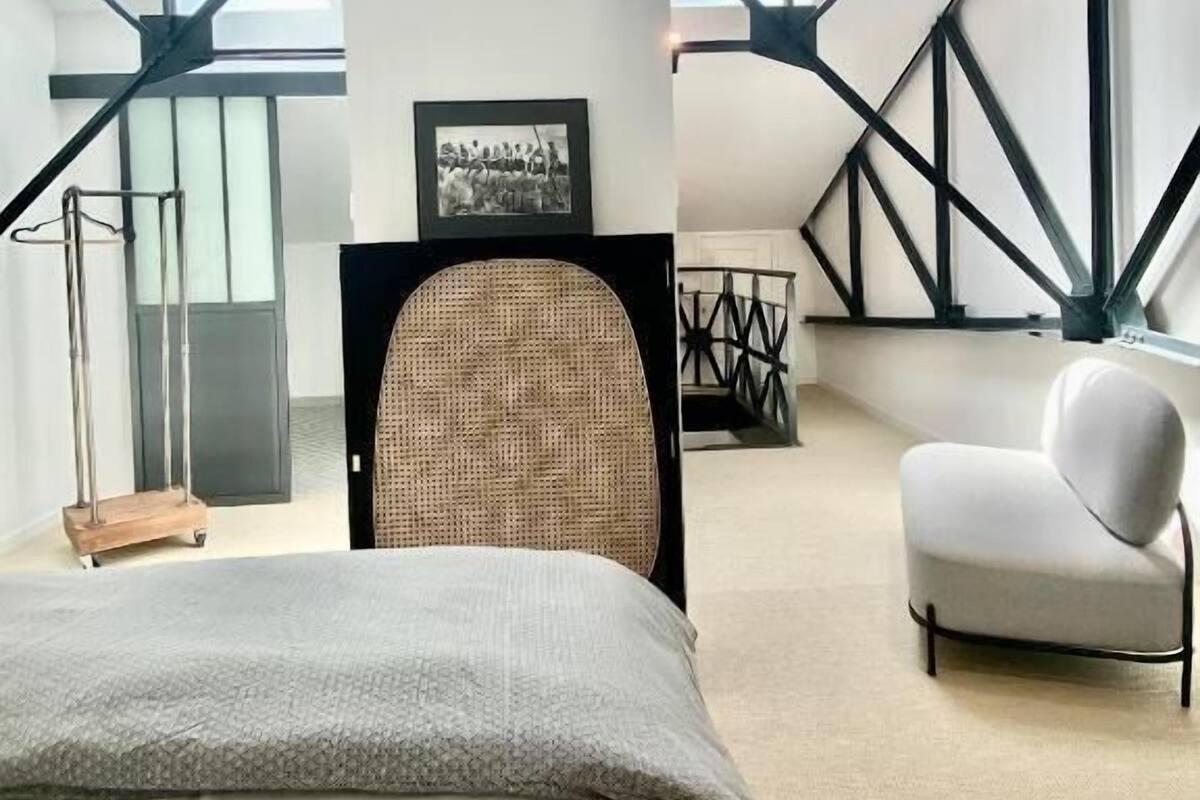 Un dormitorio moderno con una cama grande, una silla y un escritorio. Hay tragaluces y un cuadro en la pared.