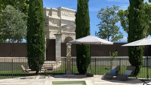 A swimming pool with lounge chairs and umbrellas, surrounded by tall trees and a stone wall. - Villa Agrippa (Orange)