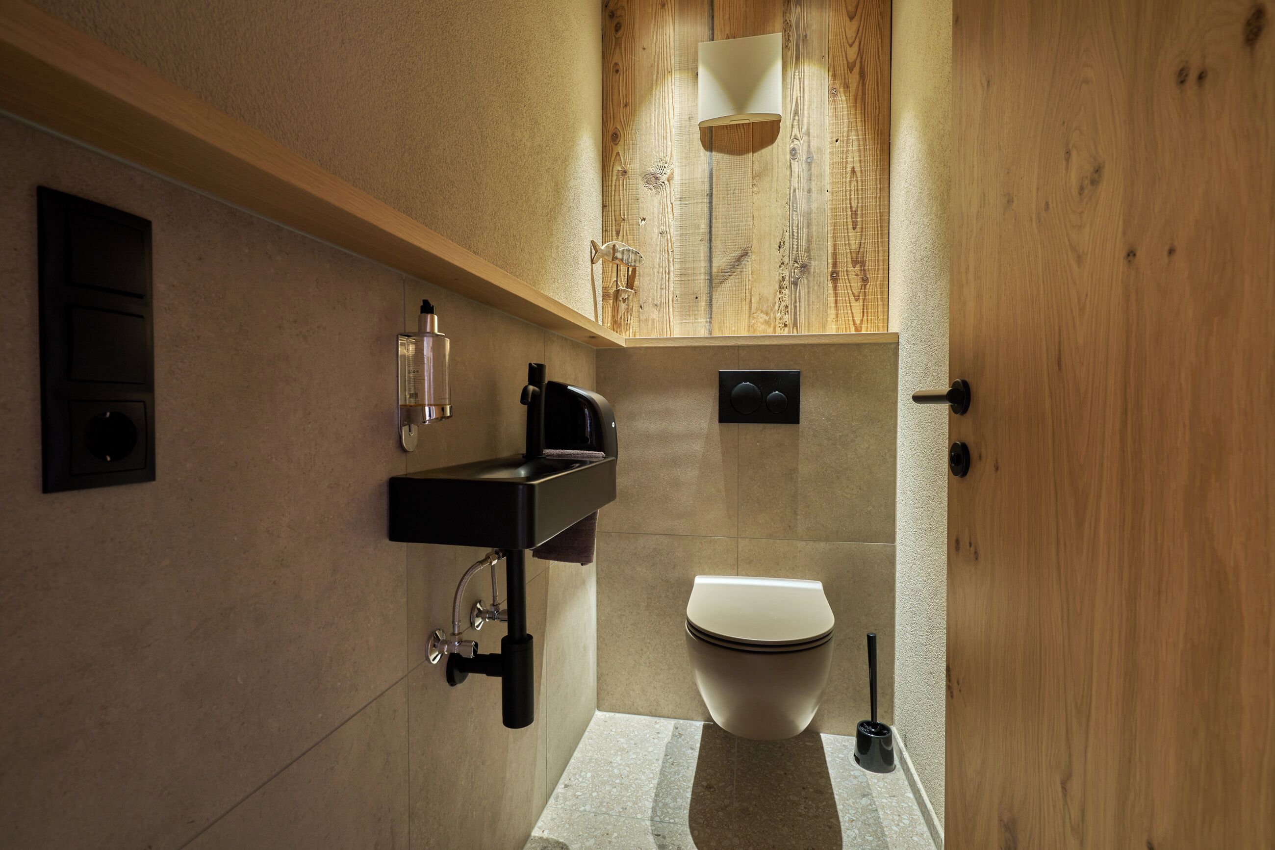 A modern bathroom with a wooden vanity, a toilet, and a sink with a soap dispenser.