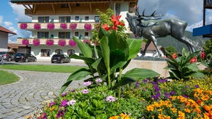 A hotel with a large outdoor statue of a deer, surrounded by colorful flowers and a cobblestone path. - Hotel Stern (Ehrwald)
