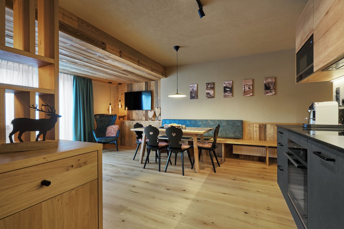 A modern kitchen with wooden cabinetry, a dining area with a bench, and a TV mounted on the wall.