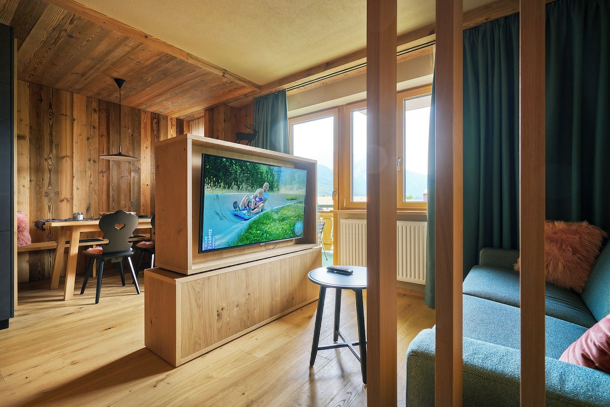 A wooden interior with a TV, a dining area, and a sofa.