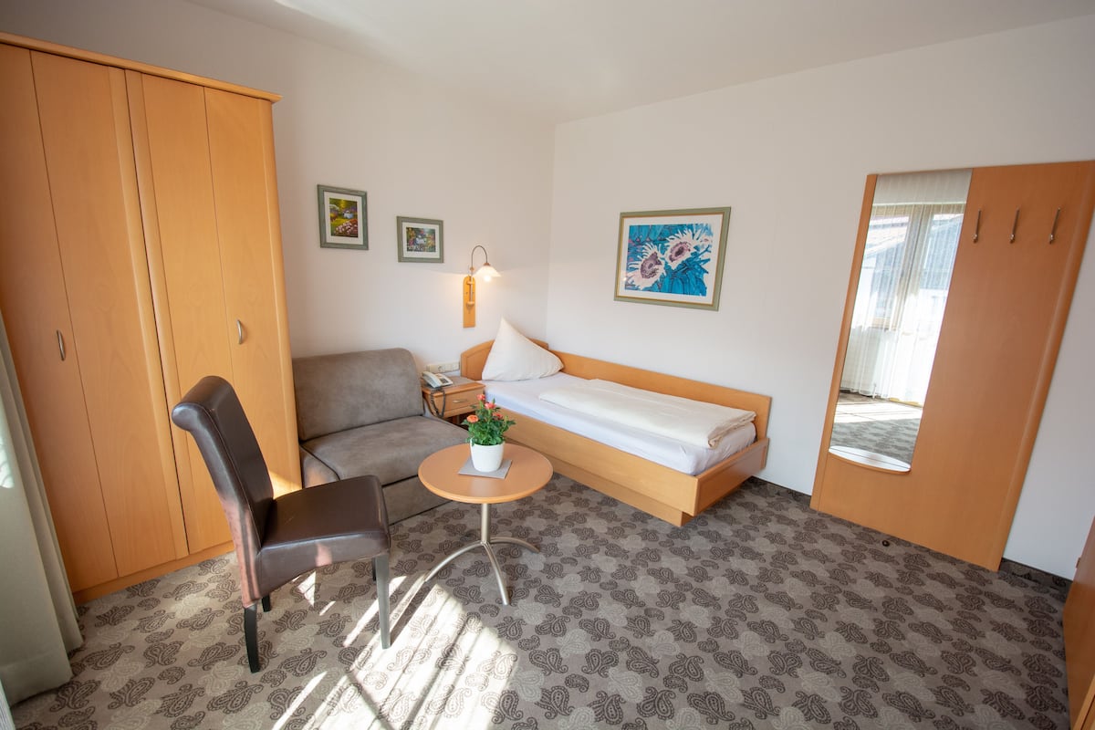 A compact bedroom with a bed, a sofa, a chair, and a small table with a plant.