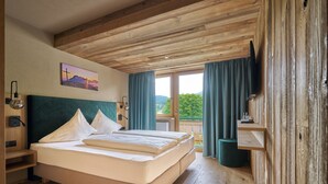 A bedroom with a wooden ceiling, a bed with white bedding, a mounted TV, and a window with curtains. - Hotel Stern (Ehrwald)