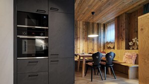 A modern kitchen with a built-in oven and microwave, wooden dining area with chairs and a bench, and a pendant light. - Hotel Stern (Ehrwald)