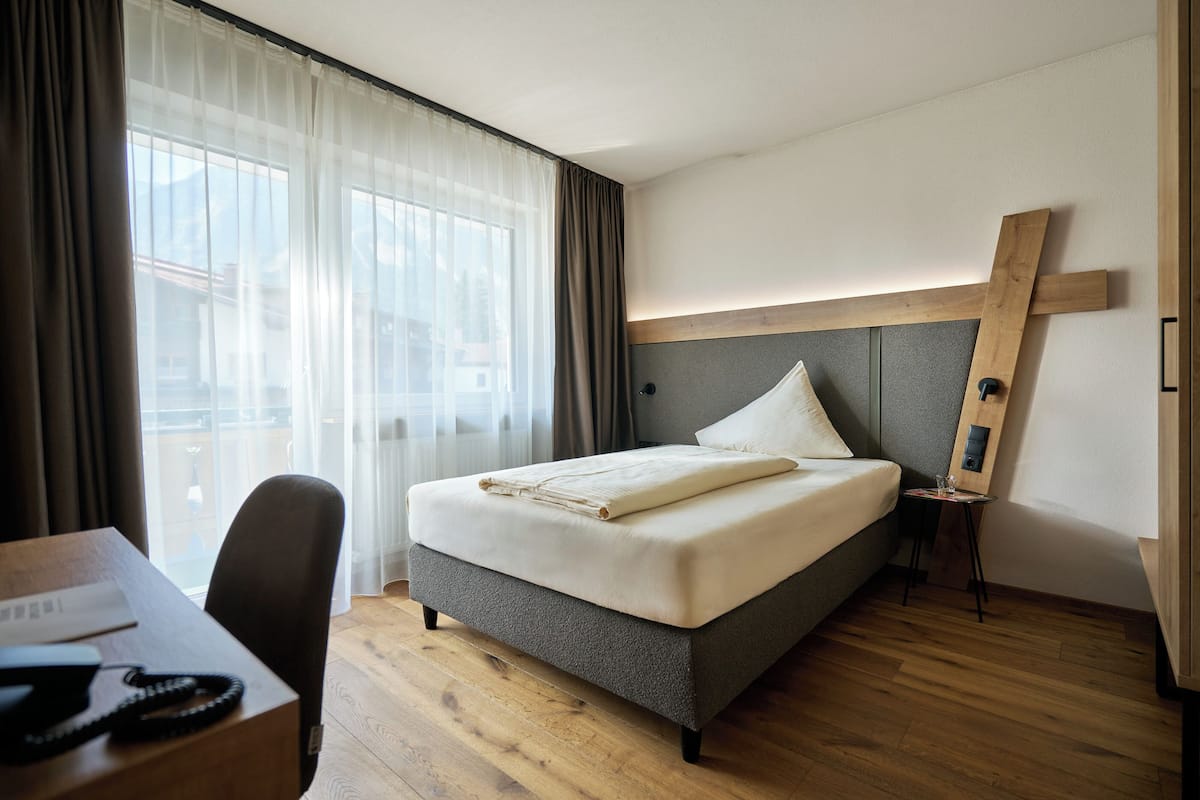 A hotel room with a bed, a desk, and a view of the outside.