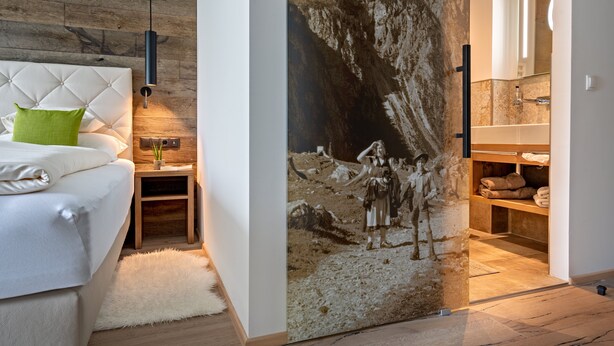 A bedroom with a large mural, a tufted headboard, a green pillow, and a nightstand with a lamp. - Hotel Stern (Ehrwald)