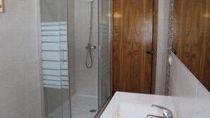 Un baño con ducha de vidrio, puerta de madera y lavamanos blanco con grifo moderno.