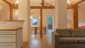 Een moderne keuken met houten balken, een zithoek met een houten tafel en stoelen, en een grijze bank in een woonruimte.