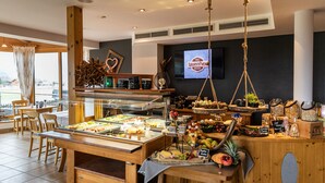 Un área de bufé con diversos alimentos, una pantalla de televisión y una barra de madera con frutas y salsas.